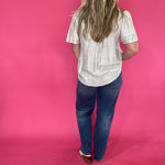 Full length view of the oatmeal V neck trapunto stitch blouse worn loose over denim