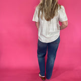 Full length view of the oatmeal V neck trapunto stitch blouse worn loose over denim