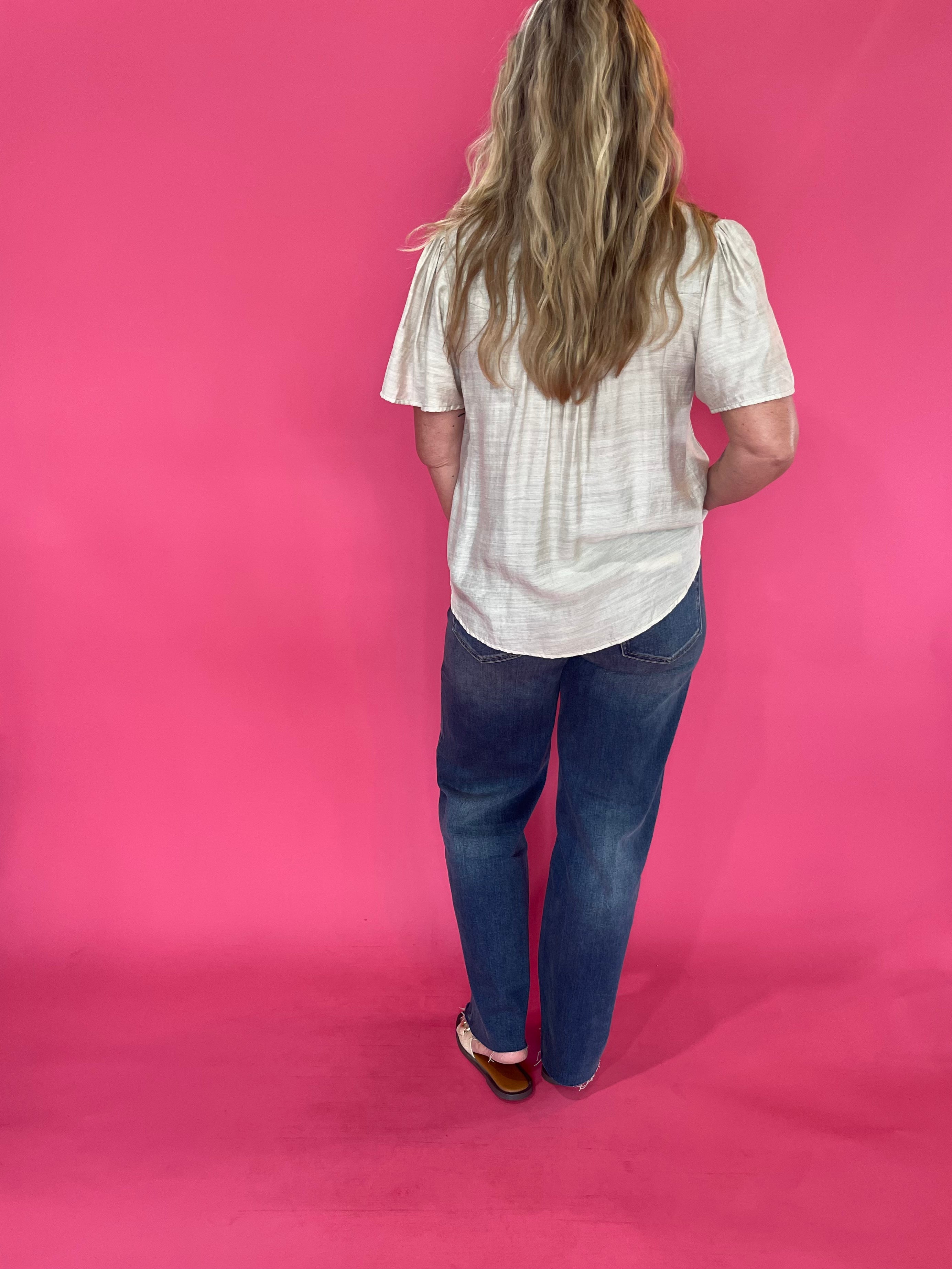 Full length view of the oatmeal V neck trapunto stitch blouse worn loose over denim