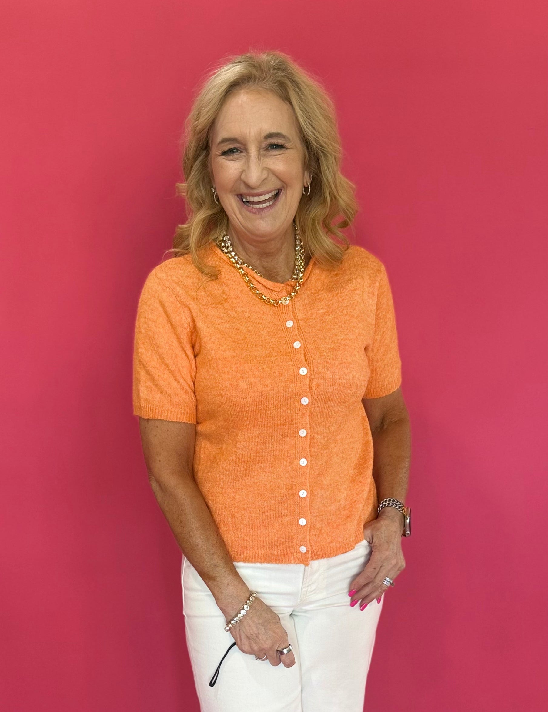 Woman wearing a tangerine orange short sleeve button cardigan worn buttoned as a top