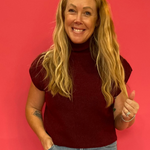 Woman wearing a wine red ribbed mock neck sweater with cap sleeves and a relaxed fit