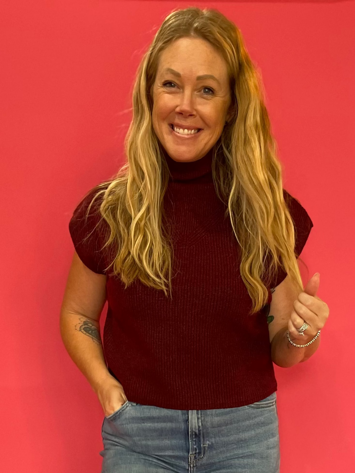 Woman wearing a wine red ribbed mock neck sweater with cap sleeves and a relaxed fit