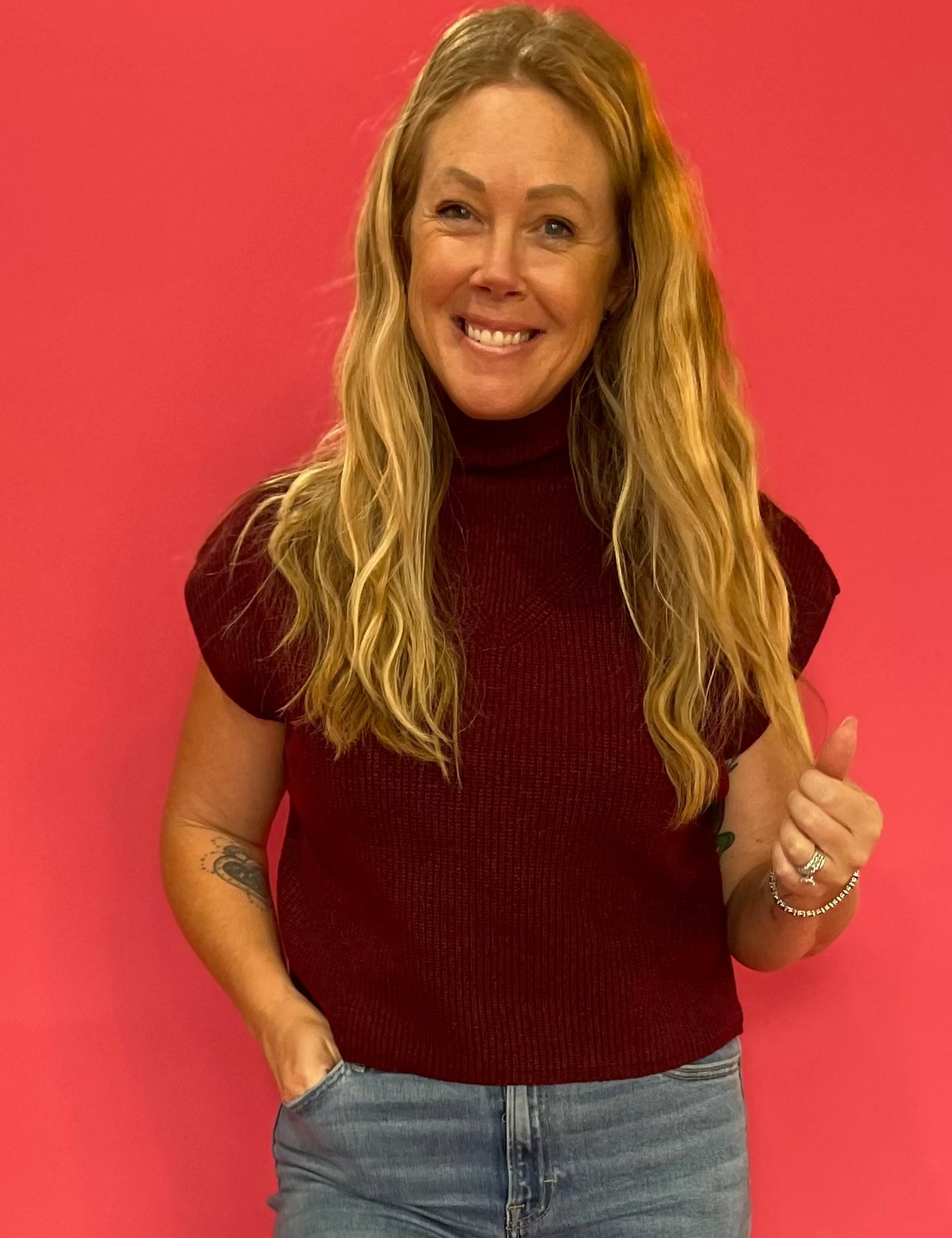 Woman wearing a wine red ribbed mock neck sweater with cap sleeves and a relaxed fit