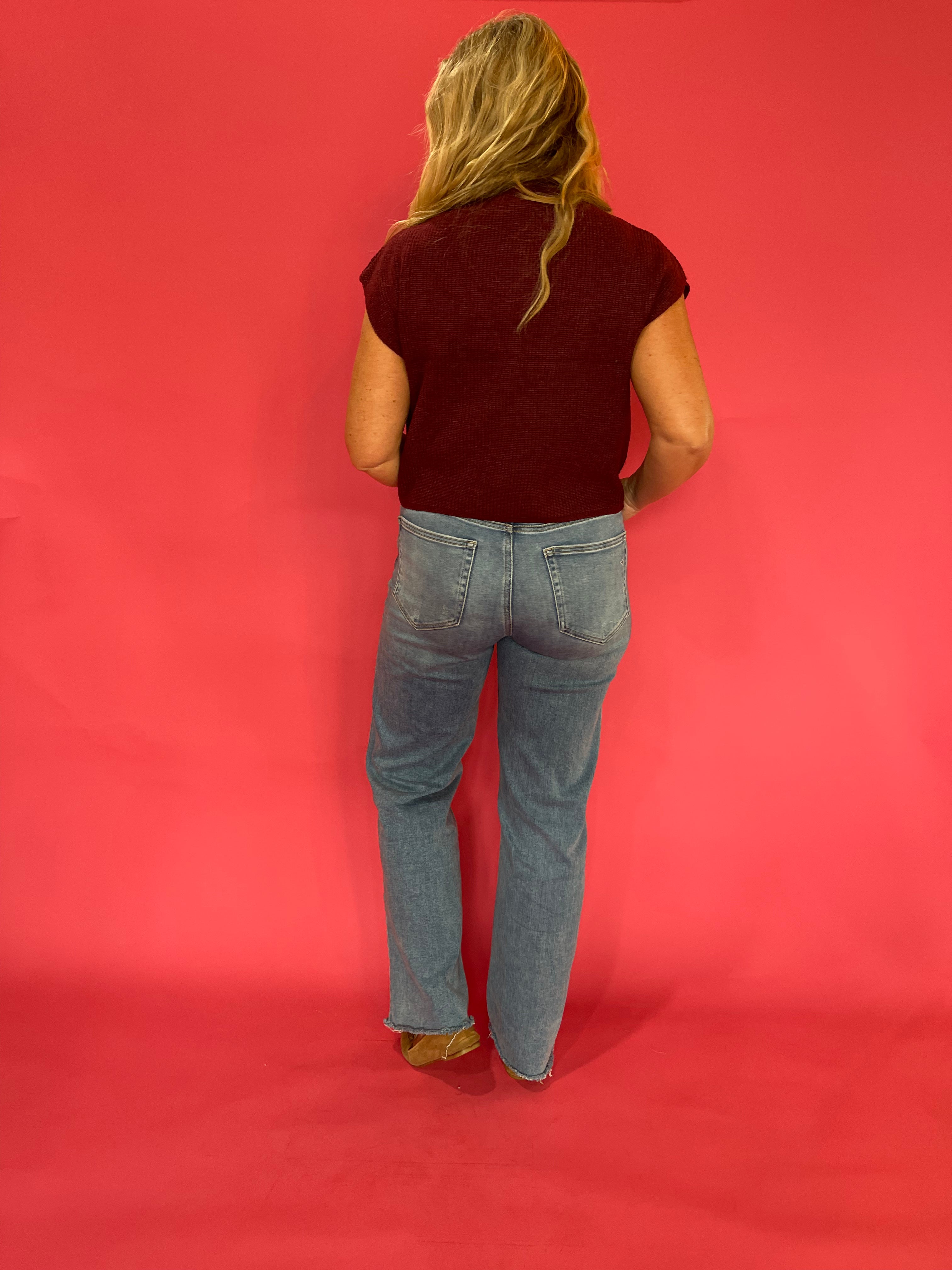 Full length view of the wine red ribbed mock neck cap sleeve sweater worn with trousers
